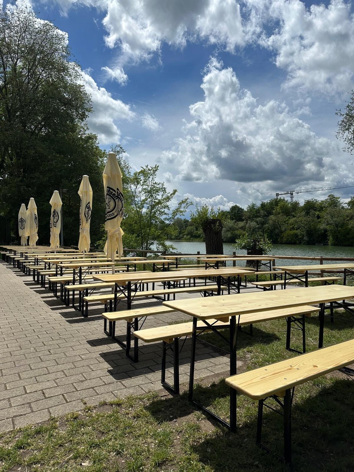 Biergarten am See mit langen Bierbänken unter dramatischem Sommerhimmel