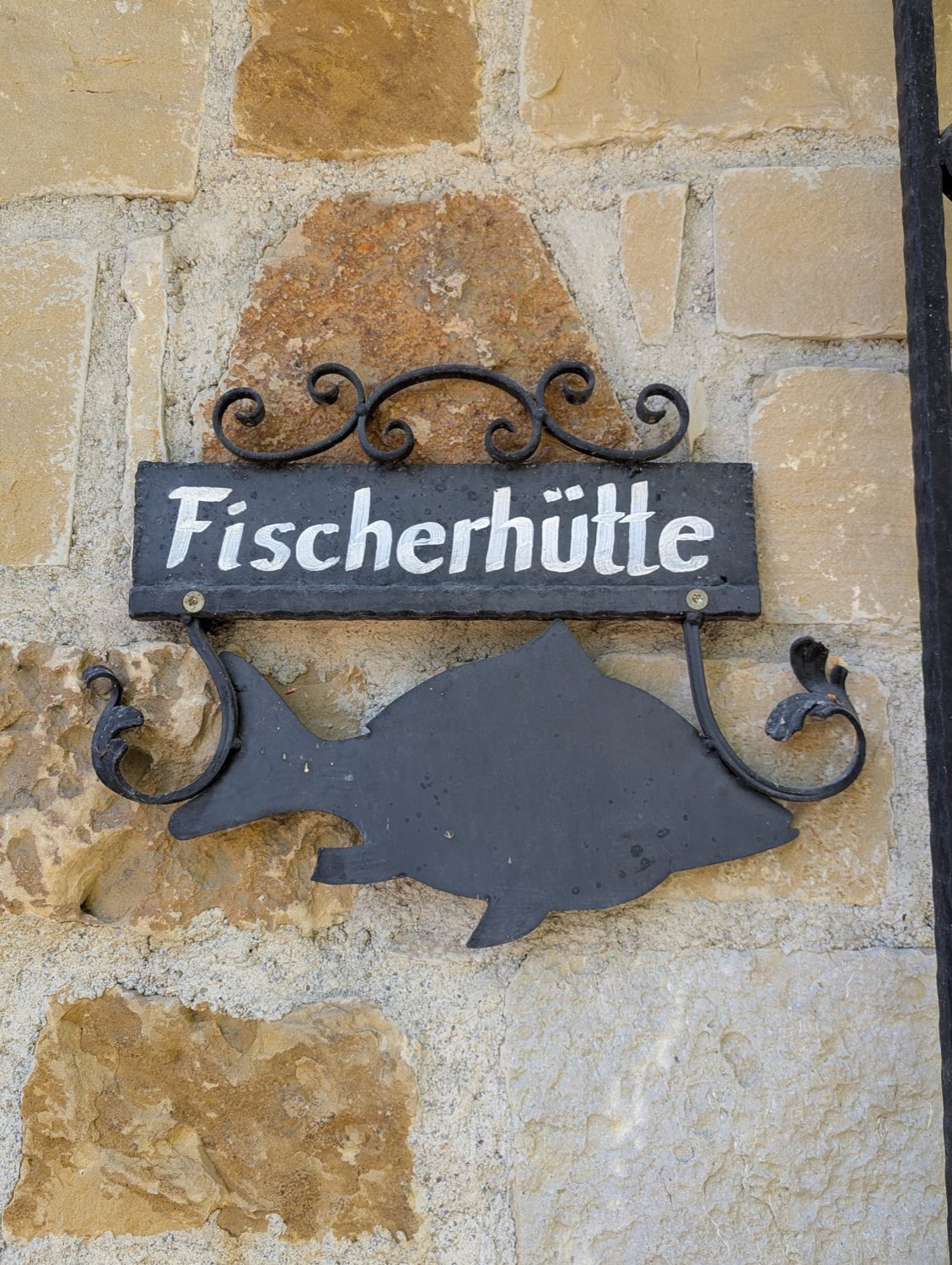 Schmiedeeisernes Fischerhütte-Schild mit Fisch an einer Steinwand